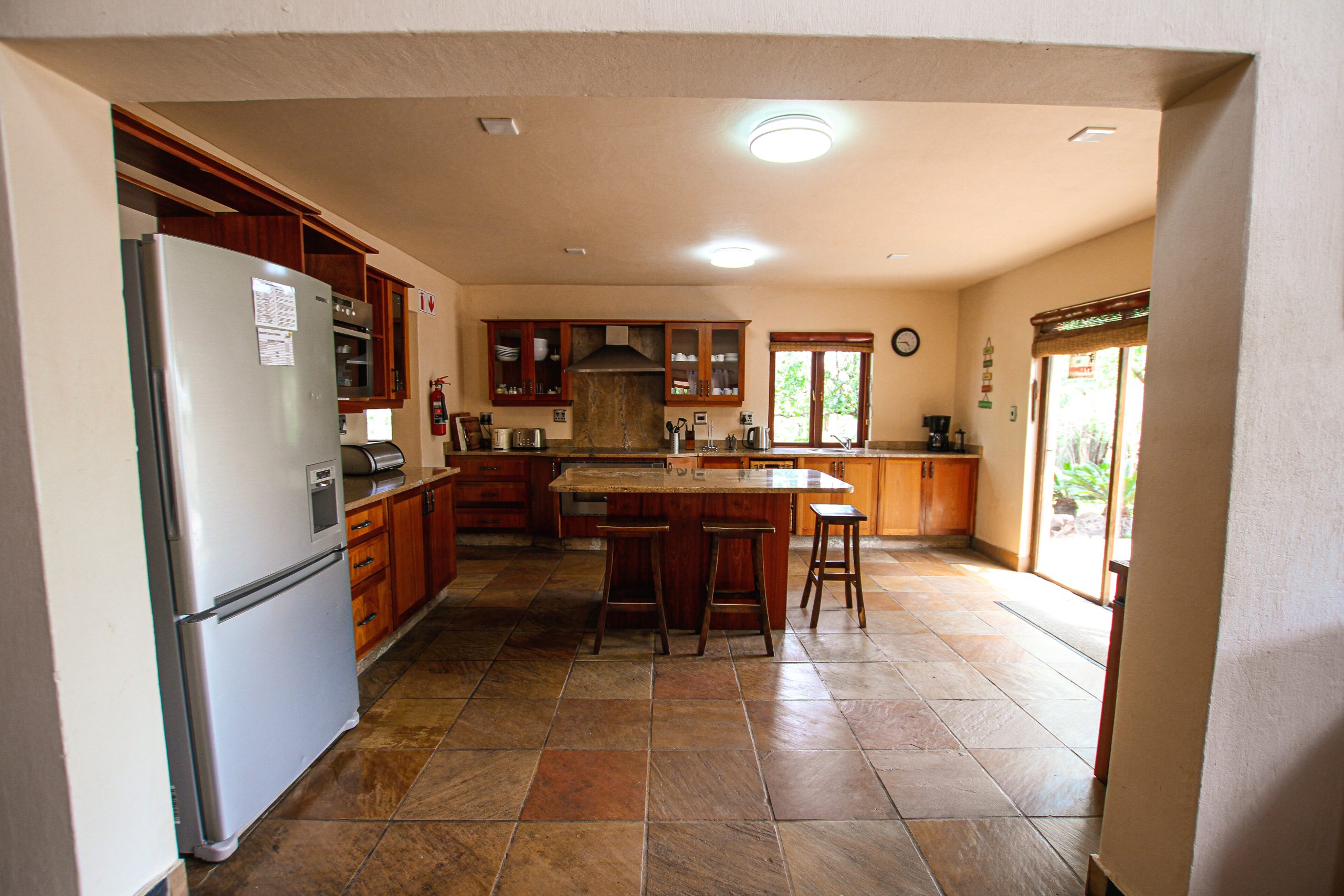 Kitchen entrance with a fridge in view and an island, colours are earthy tones