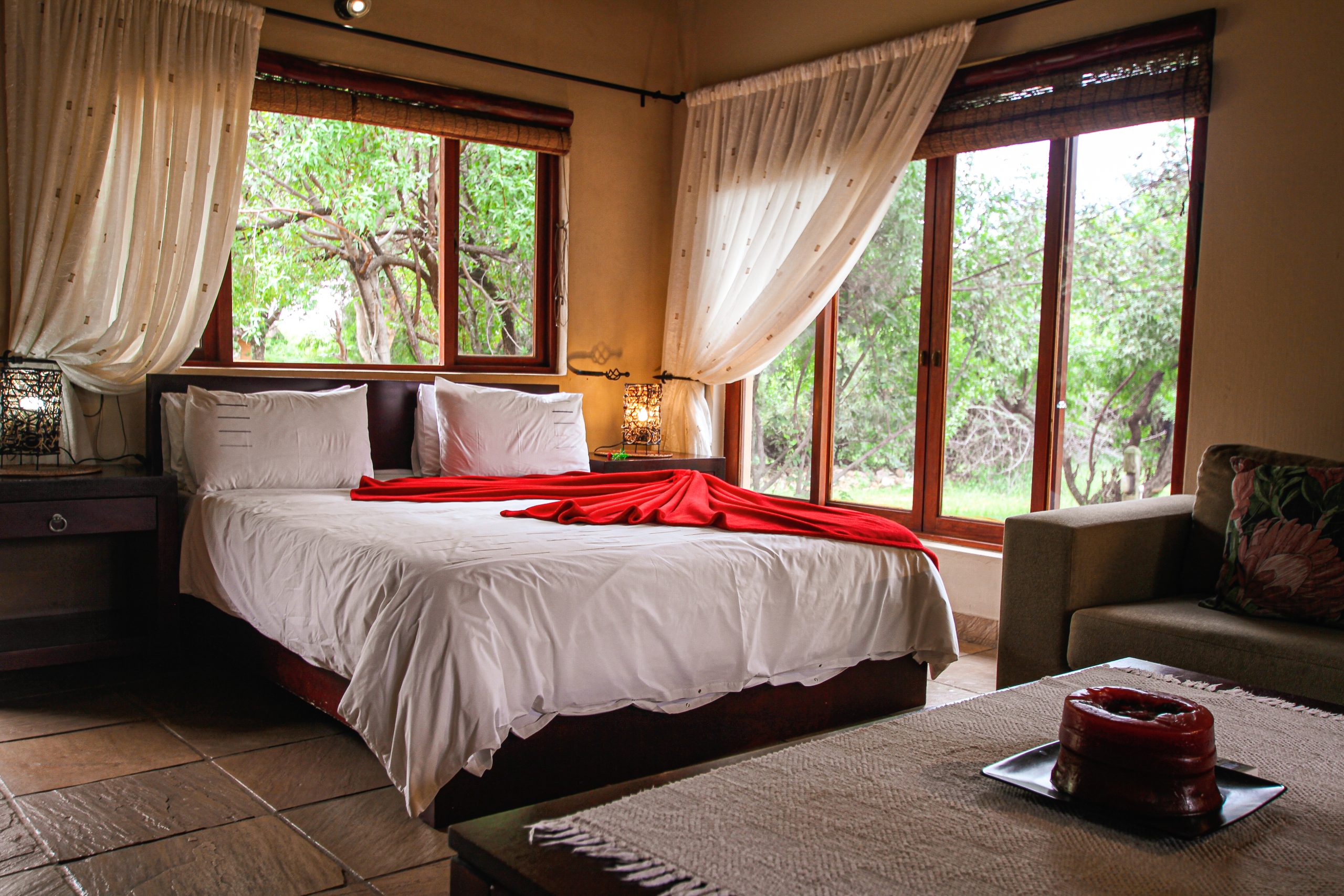 Chalet bed, covered in white linen and red throw. Big windows around the room